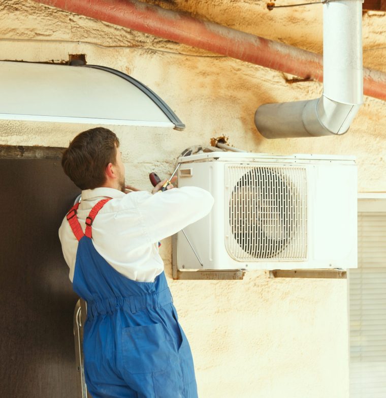 HVAC technician working on a capacitor part for condensing unit. Male worker or repairman in uniform repairing and adjusting conditioning system, diagnosting and looking for technical issues.